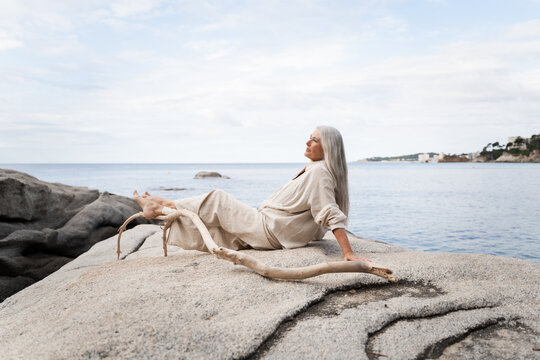 Woman Sitting on Rock Near Sea in Coastal Location During Daytime
