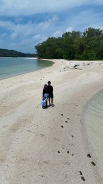 A couple walks along the white sandy beach at Kerayaan Beccu Beach and smiles at the camera