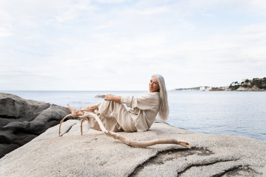 Woman Sits on Rocks by the Water in a Coast