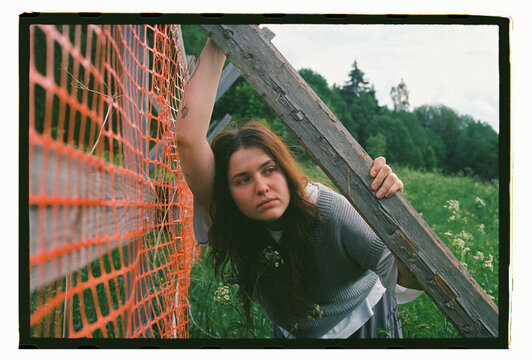 A young woman grips a weathered wooden beam in overgrown fields
