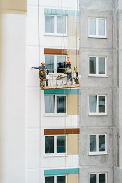 Workers paint the wall of a high-rise building.