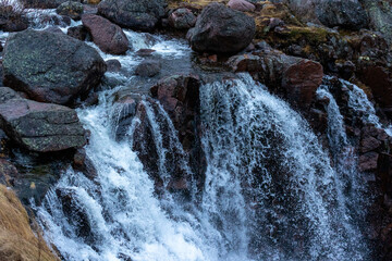 Close-up view of powerful waterfall cascading rapidly over dark wet rocks and red granite stones in wild nature. © AndreyZayats