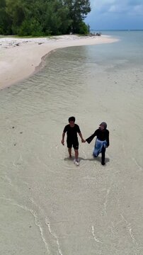 A couple walks along the white sandy beach at Kerayaan Beccu Beach and smiles at the camera