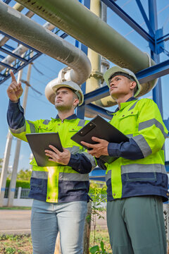 Industry specialists inspect massive piping at a gas-fired power plant integrated with a petroleum and oil refinery complex, focusing on maintenance for energy generation safety and efficiency.