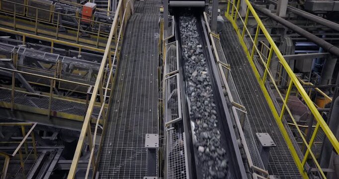 Concentration factory for copper, gold, magnetite concentrate. Conveyor belt with ore moving along inclined metal walkway inside industrial processing plant.