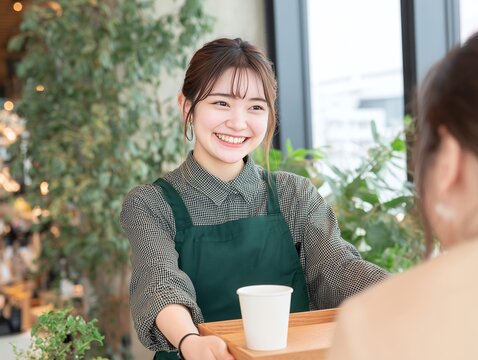 笑顔で接客するカフェの女性スタッフがお客様へドリンクを提供