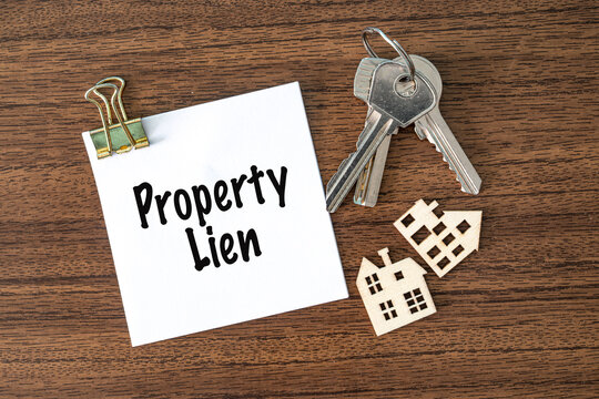 Property Lien text on white paper with keys and toy houses on wooden desk, real estate finance and law concept