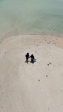 A couple walks along the white sandy beach at Kerayaan Beccu Beach and smiles at the camera