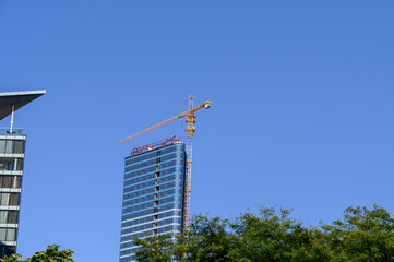 Contemporary glass skyscraper under construction against a clear blue sky. Concept of sustainable urban development, smart city infrastructure, and energy-efficient architecture in a growing city © GRON777