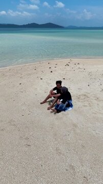 A couple walks along the white sandy beach at Kerayaan Beccu Beach and smiles at the camera