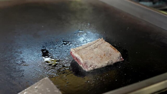 searing raw beef steak cut on flat top grill in restaurant kitchen