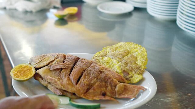 serving fried fish with patacon and lemon slice on tray in restaurant kitchen