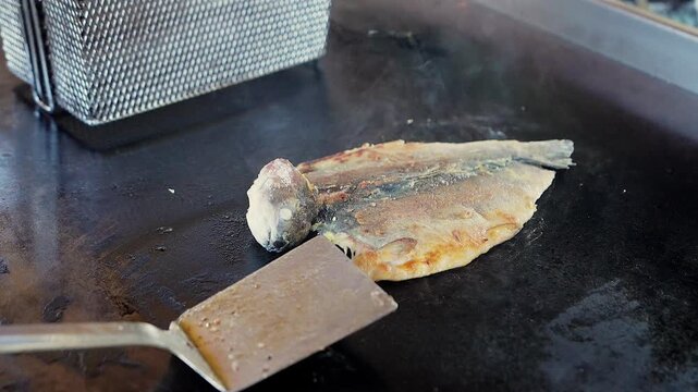 cooking boneless trout fish on flat top grill with spatula in restaurant kitchen