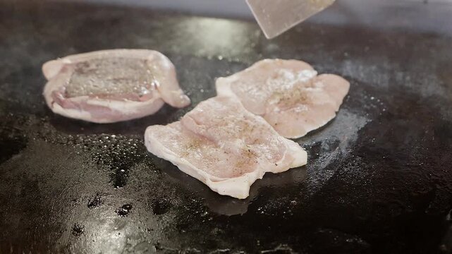 cooking meat cutlets on flat top grill in restaurant kitchen