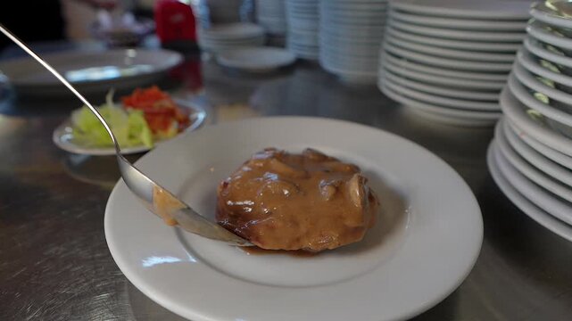 pouring mushroom gravy over cooked meat dish in restaurant kitchen