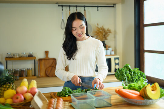 Young Woman Chopping Fresh Kale in a Modern Home Kitchen with Colorful Vegetables and Fruits