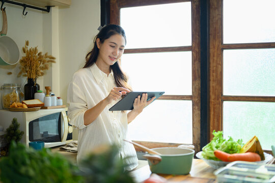 Young Woman Using Tablet While Cooking in a Bright Home Kitchen with Fresh Vegetables
