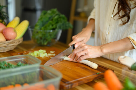 Woman Chopping Green Onion on Wooden Cutting Board with Fresh Vegetables in Home Kitchen