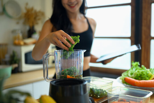 Young Woman Adding Kale to Blender for Healthy Green Smoothie in Home Kitchen