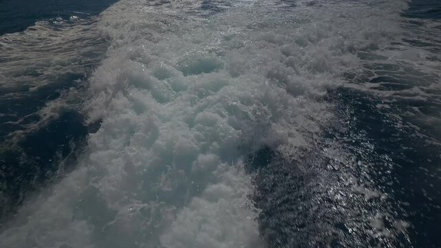 Turbulent white foam water trail behind a large boat in a calm blue sea on a sunny day, slow motion