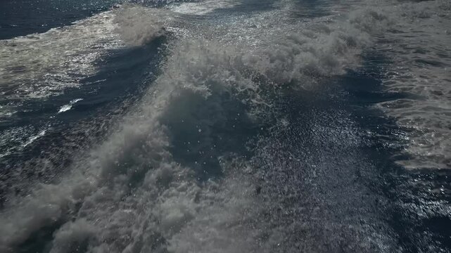 Turbulent white foam water trail behind a large boat in a calm blue sea on a sunny day, slow motion