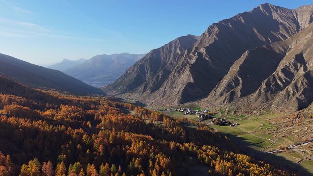 Aerial view of the Crevoux valley with golden larch forest, the village of La Chalp, and mountain landscape in autumn. Hautes-Alpes, France