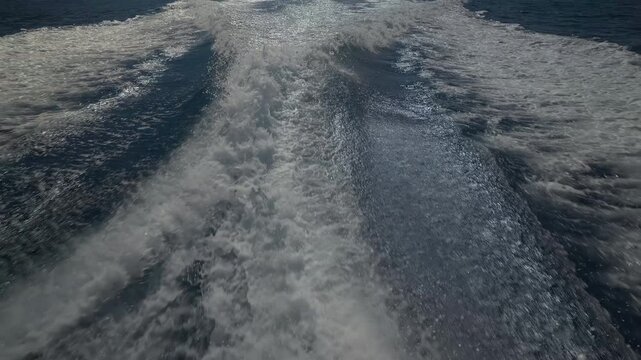 Turbulent white foam water trail behind a large boat in a calm blue sea on a sunny day, slow motion