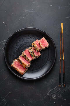 Seared grilled tuna steak tataki slices sesame seeds lemon black plate healthy delicacy
