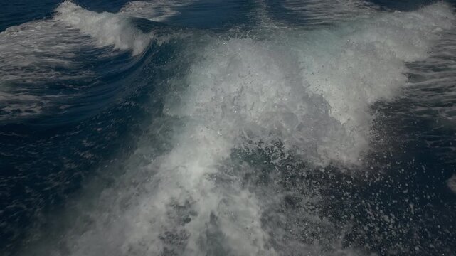 Turbulent white foam water trail behind a large boat in a calm blue sea on a sunny day, slow motion
