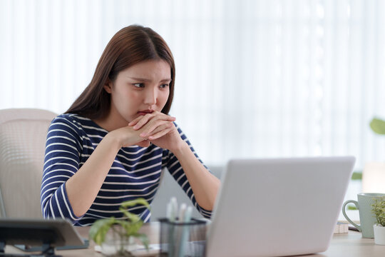 Young Asian woman looking anxious and stressed while working on laptop in bright home office with copy space
