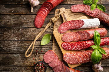Fototapeta na wymiar Set of different types of sausages, salami and smoked meat with basil and spices on wooden background. Top view.