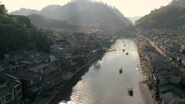 Horizontal 4K UHD aerial drone shot performing 180 degree rotation over Tuojiang River showing traditional wooden houses and historical architecture in Fenghuang Ancient Town Hunan China