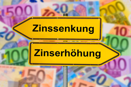 Zwei Wegweiser &uuml;ber vielen Euro-Banknoten zeigen in gegens&auml;tzlicher Richtung und sind beschriftet mit Zinssenkung und Zinserh&ouml;hung