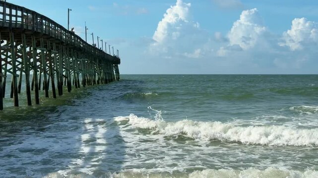 Ocean waves breaking beside a wooden fishing pier at the beach with copy space