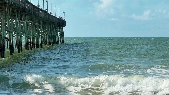 Ocean waves breaking beside a wooden fishing pier at the beach with copy space