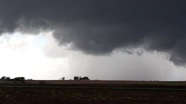 A rotating wall cloud hangs beneath a severe storm in the sky over farmland. Time lapse.