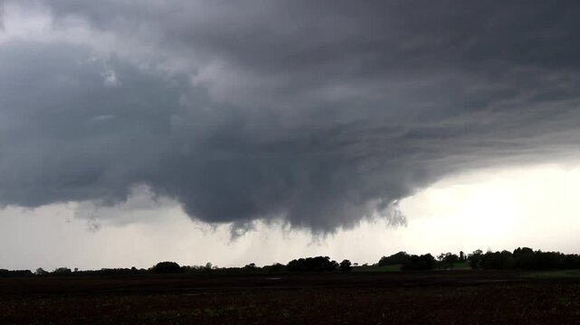 Time lapse footage of a funnel cloud and rotating wall cloud on a severe storm passing over farmland.