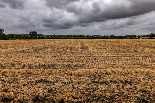 Plowed agricultural field with straw stubble after harvest under a dramatic stormy sky
