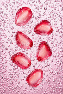 Fresh pomegranate arils surrounded by sparkling bubbles in a vibrant macro composition. Bright healthy food background with refreshing texture.