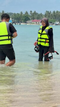A young couple on the beach is preparing to go swimming with snorkeling gear on a sunny day