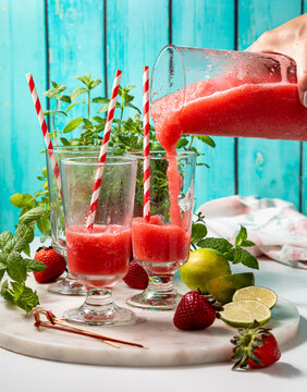 Pouring a fresh batch of strawberry daiquiri mocktails into frosty glasses.