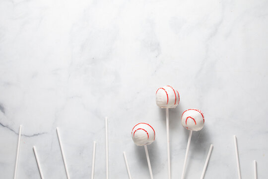Decorated cake pops with white sticks against a white marble surface.