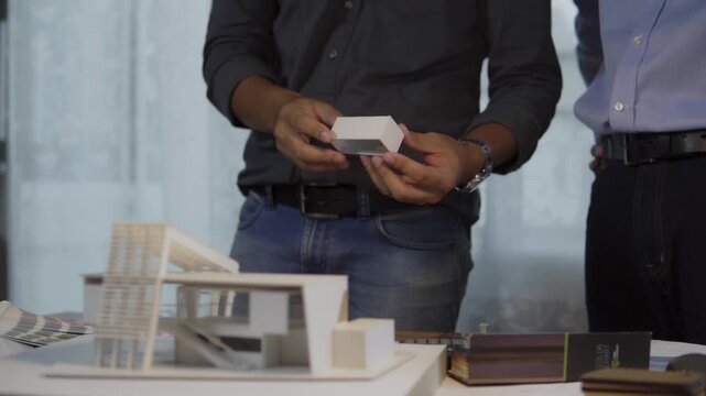 Male architects holding building section examining architectural scale model while discussion in office. concept of architectural design team collaboration construction planning building structure.
