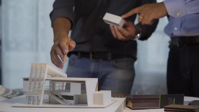 Male architects pointing and holding building section examining architectural scale model while discussion in office. concept of architectural design team collaboration construction planning team.