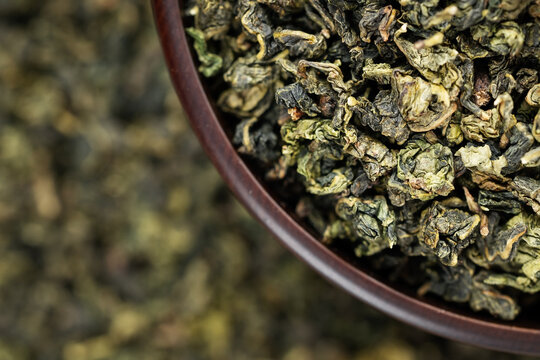 Dark wooden bowl filled with Tieguanyin on tea texture background