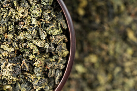 Wooden cup full of green oolong surrounded by loose tea texture