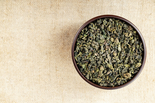 Rustic wooden bowl filled with Tie Guan Yin on beige burlap texture