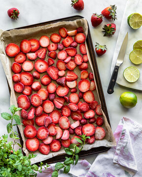 A parchment lined baking sheet with frozen strawberry slices for flash freezing.