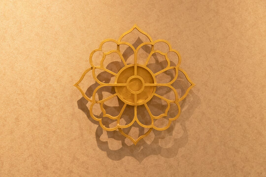 An elegant golden lotus flower mandala wall ornament mounted on a warm-toned textured wall, featuring soft shadows and a luxurious aesthetic, ideal for interior design and background concepts.
