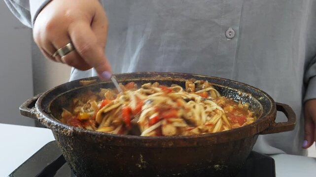 Vegetables with chicken and udon are stewed in a frying pan in Pad Thai sauce and spices stirred with a spoon. Medium plan.